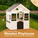 White wooden playhouse with black trim in a garden setting, featuring the brand 'Avenlur'.