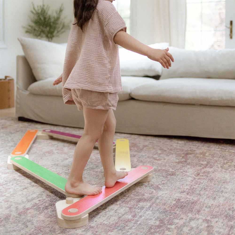 Child standing on a colorful balance beam in a living room.