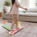 Child standing on a colorful balance beam in a living room.