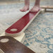 Wooden balance beam with red top and brown bottom on a patterned rug.