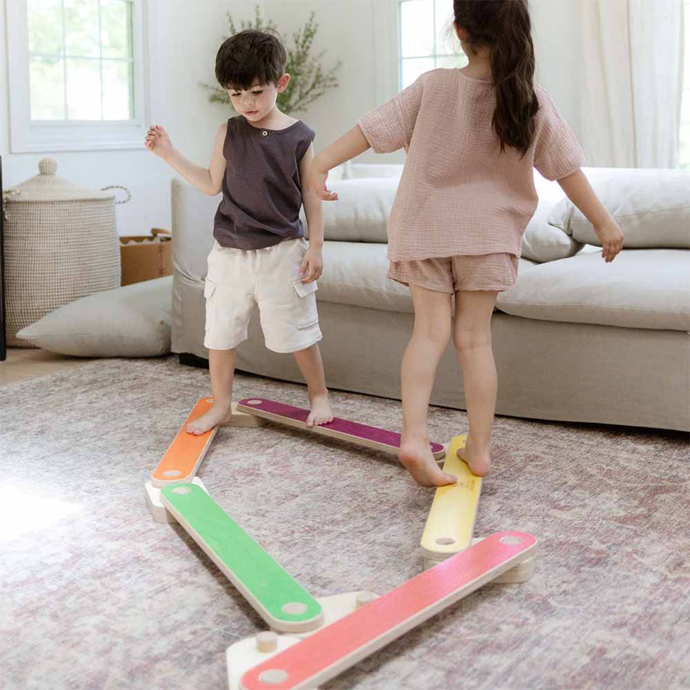 Two children playing with a colorful balance beam in a living room.