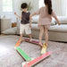 Two children playing with a colorful balance beam in a living room.