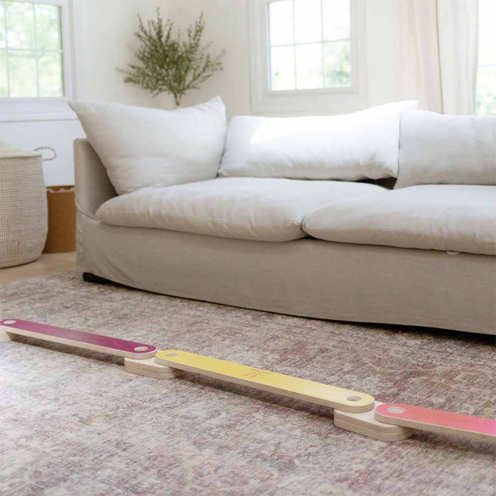 Colorful wooden balance beam on a carpeted floor with a beige sofa in the background.
