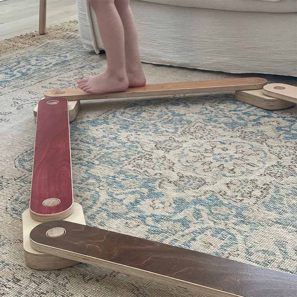 Child standing on a balance beam on a patterned rug