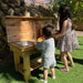 Two children playing with a wooden play kitchen set outdoors.