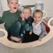 Three children sitting inside a wooden wobble board.