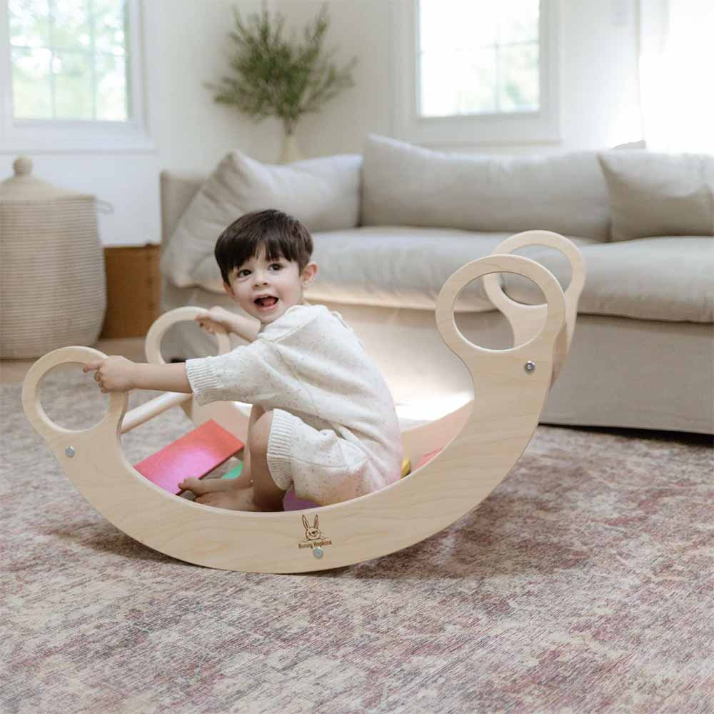 Child playing on a wooden rocking toy in a living room.