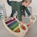 Child playing on a colorful wooden rocker in a room with shelves and toys.