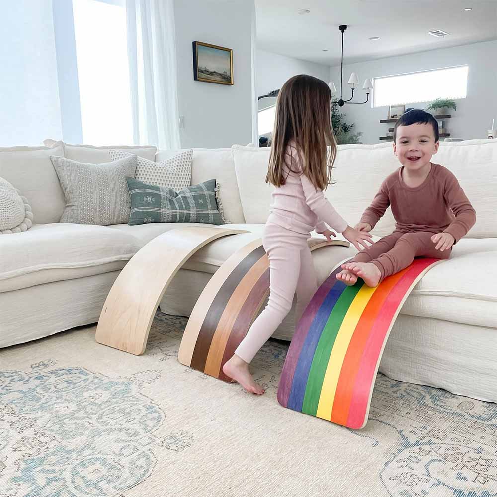 Two children playing on colorful, curved boards in a living room.