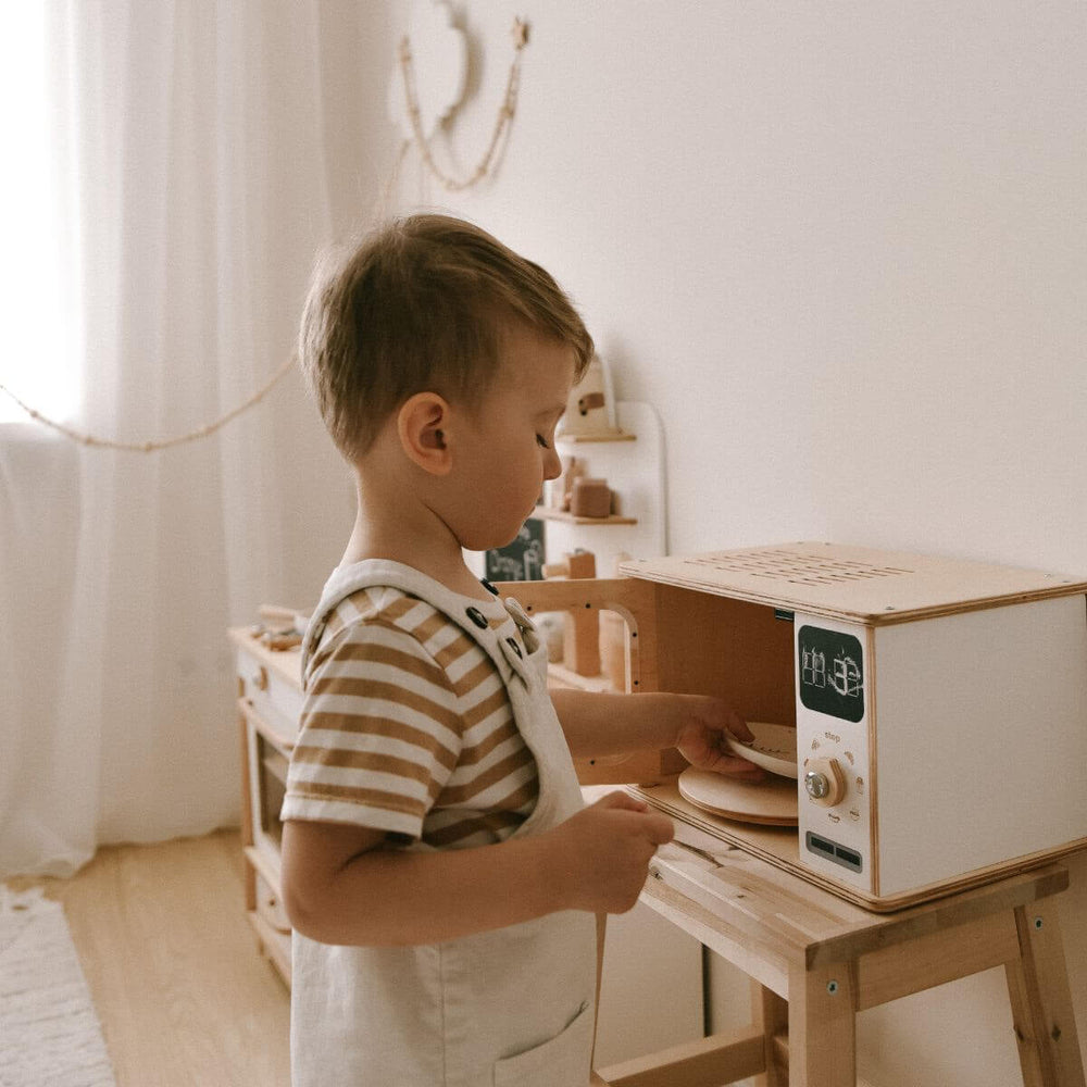 Child playing with a wooden toy kitchen set in a cozy room.