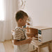 Child playing with a wooden toy kitchen set in a cozy room.