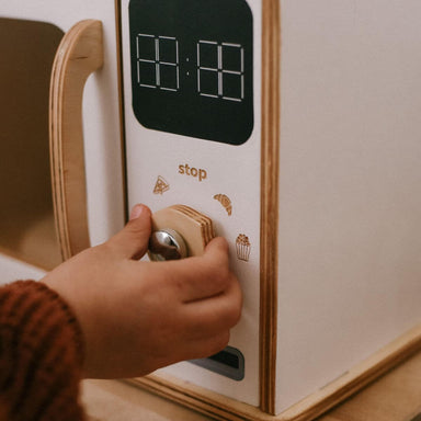 Hand pressing a button on a toy microwave appliance with a clock display.