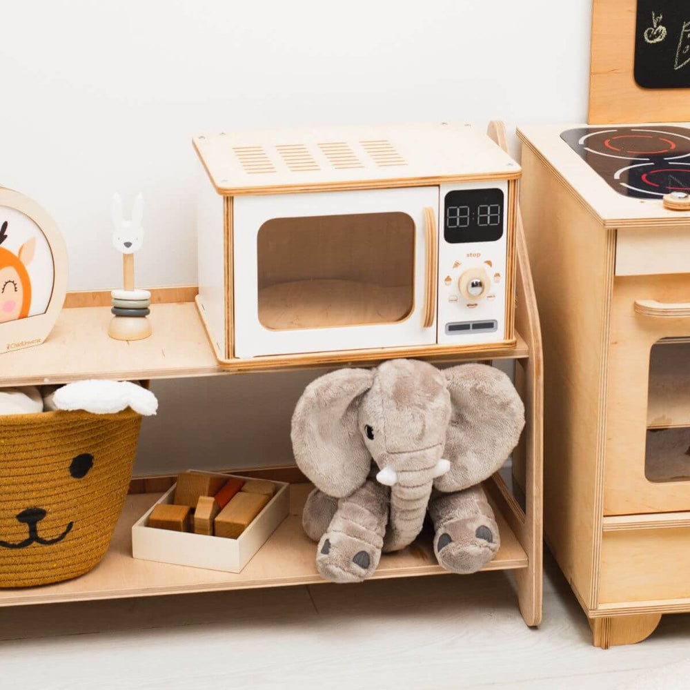 Children's play kitchen set with toy stove, microwave, and elephant plush toy on a shelf.