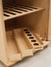 Wooden play refrigerator with multiple compartments on a light wooden floor.
