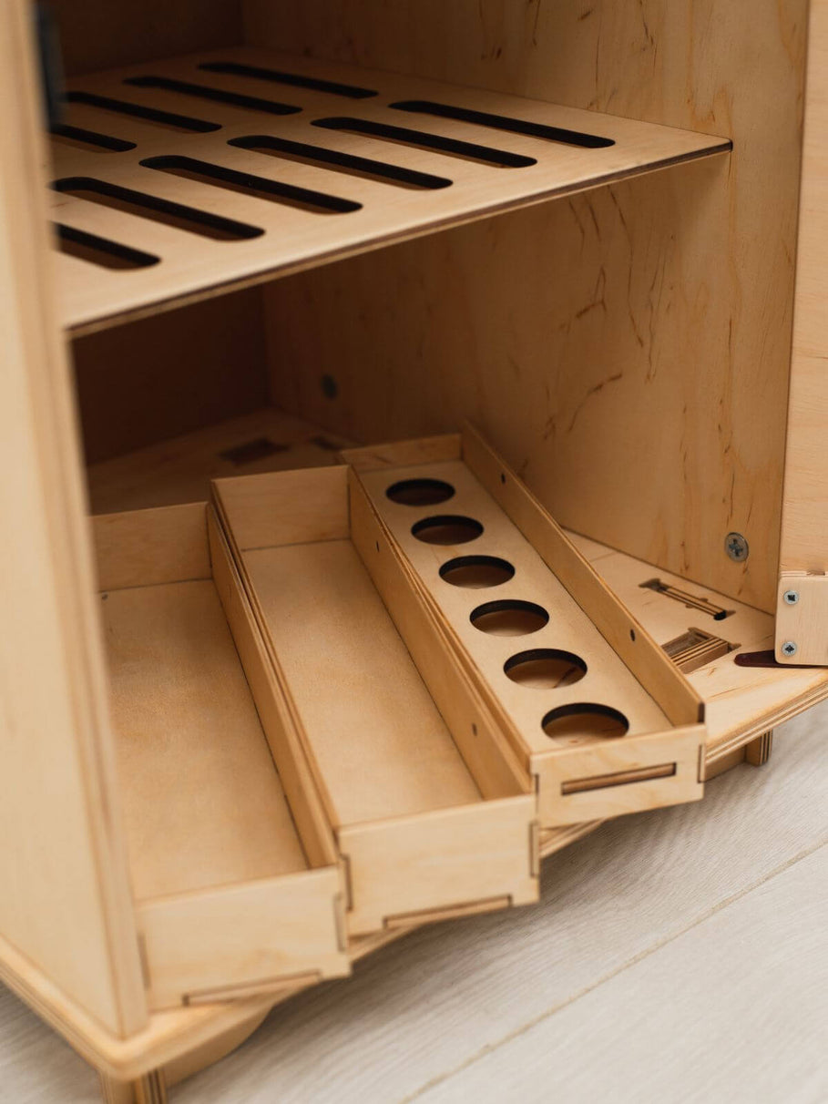 Wooden play refrigerator with multiple compartments on a light wooden floor.
