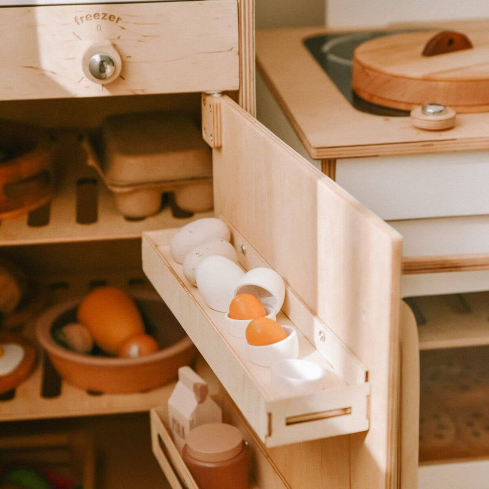 Wooden toy kitchen set with a fridge compartment open, showing eggs and bottles.