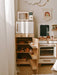 Wooden play kitchen set with various appliances and shelves in a room setting.