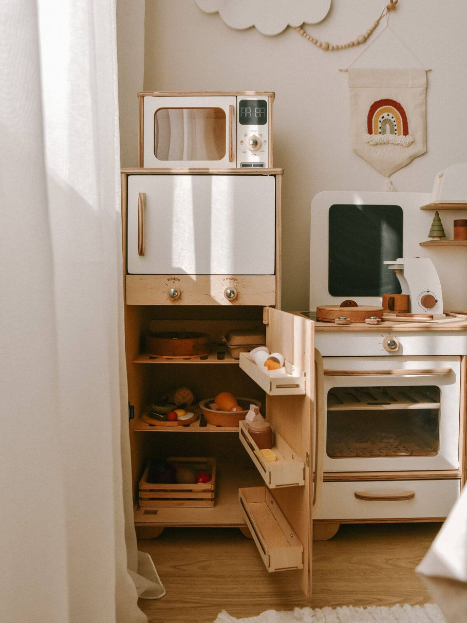 Wooden play kitchen set with various appliances and shelves in a room setting.