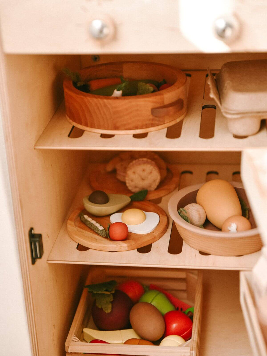 Wooden toy refrigerator with shelves containing toy food items.