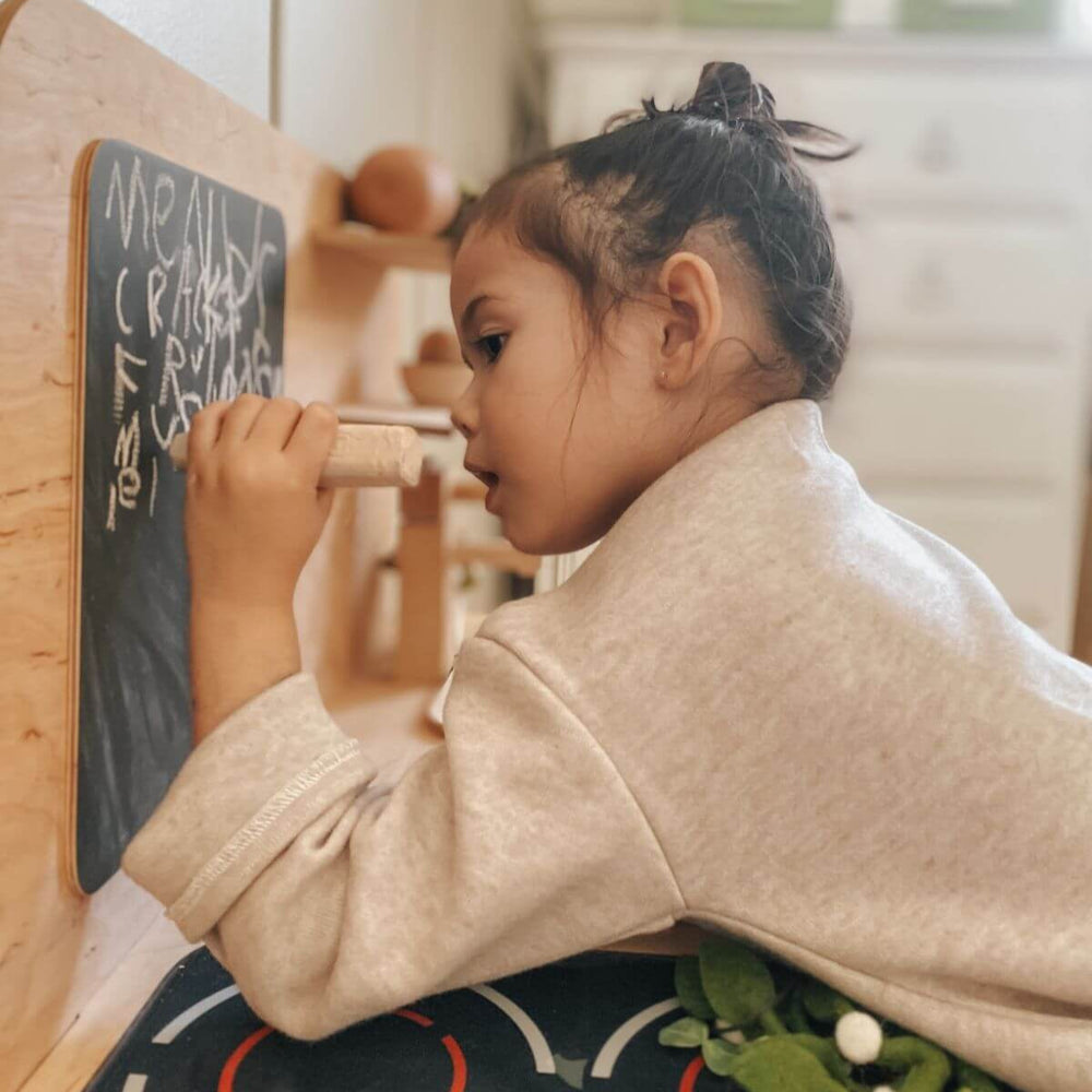 Child writing on a small chalkboard with wooden furniture in the background