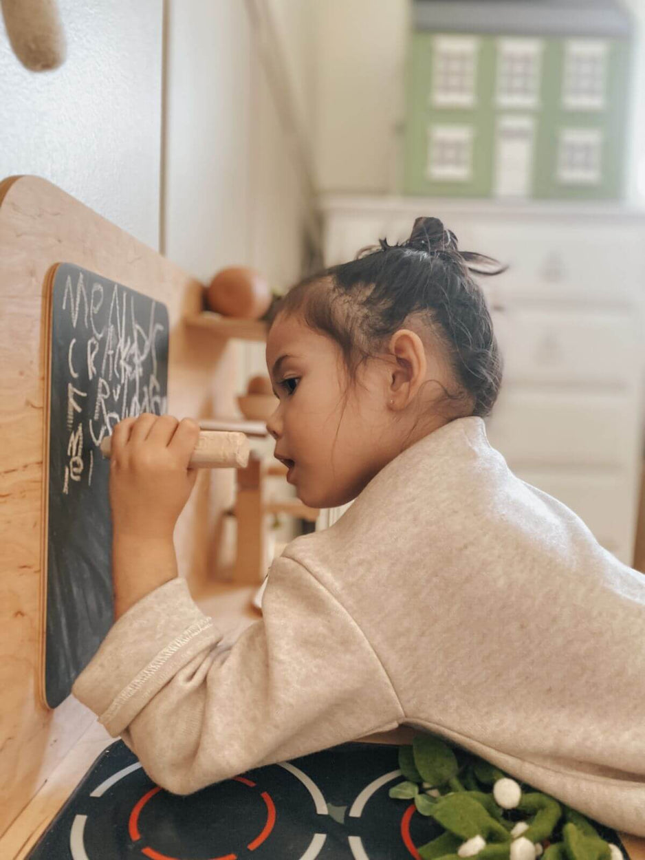 Child writing on a small chalkboard with wooden furniture in the background