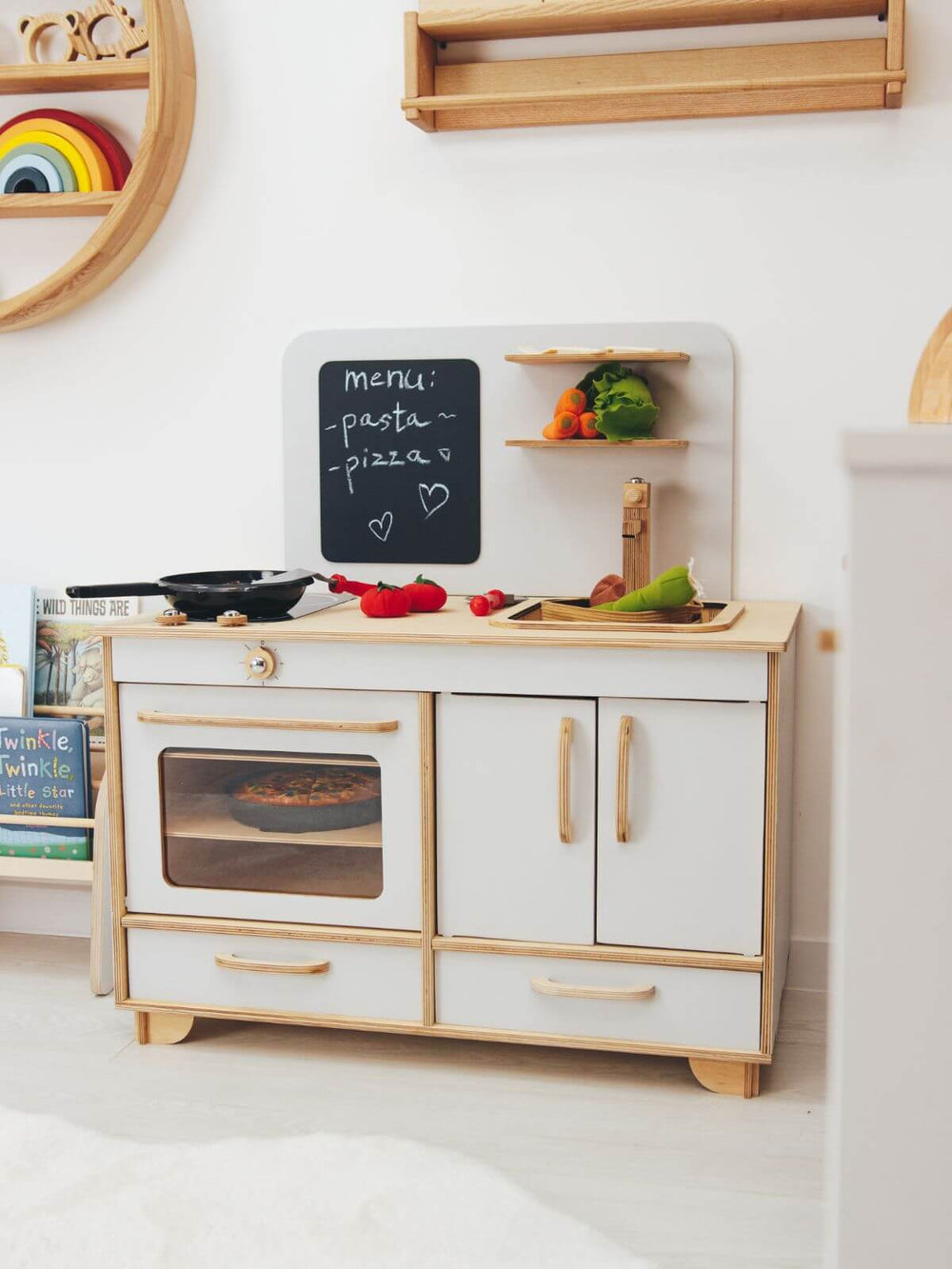 Children's play kitchen set with oven, shelves, and pretend food on a white wall background.