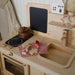Wooden play kitchen set with stove, sink, and toy items on a neutral background
