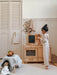Child playing with a wooden play kitchen set in a room with white walls and wooden furniture.