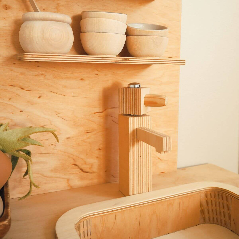 Wooden toy kitchen fixtures including a faucet and shelves with bowls on a wooden wall.