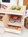 Children's play kitchen set with toy pots, pans, and utensils on a wooden shelf.