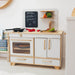 Wooden play kitchen set with oven, cabinets, and a chalkboard menu on a white wall.