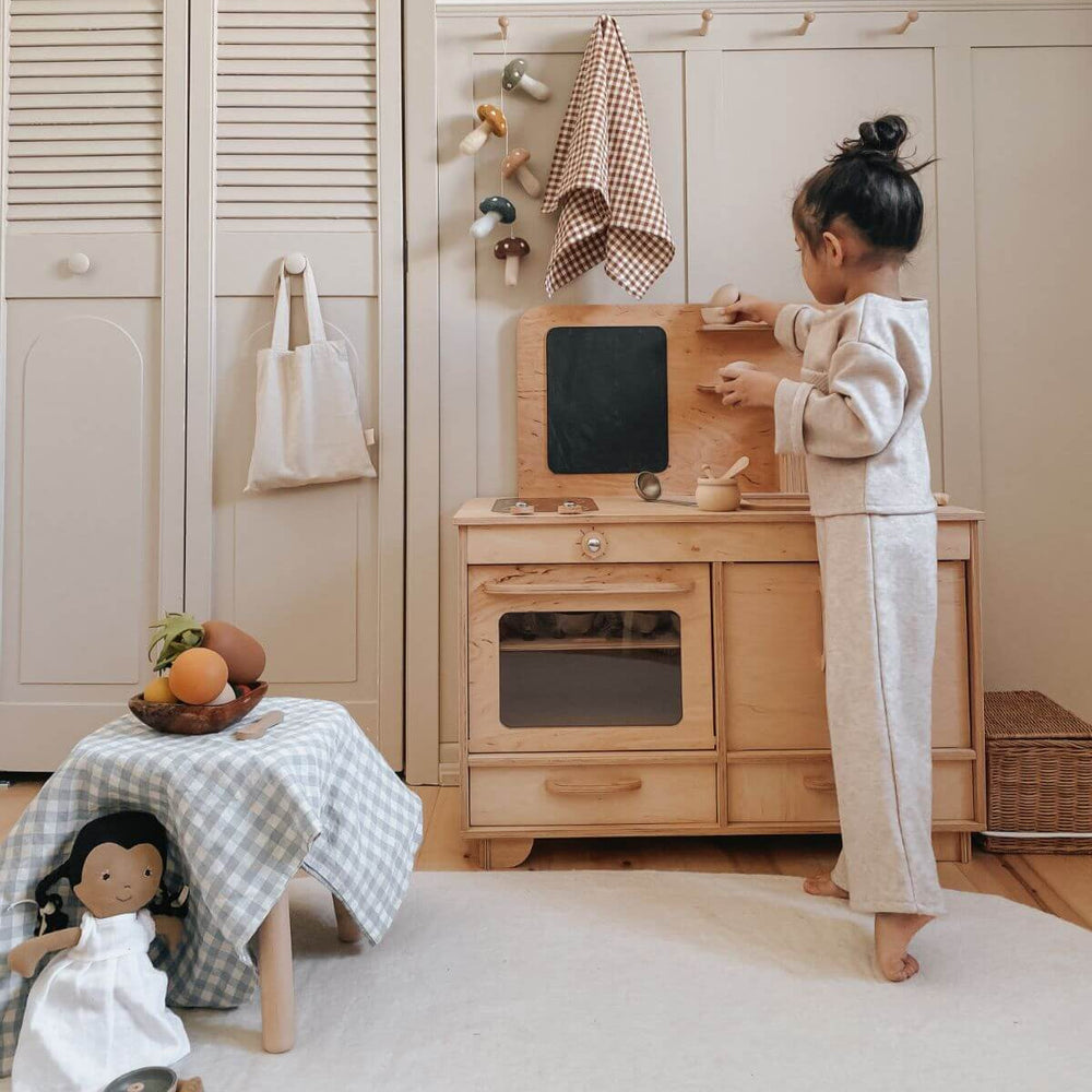 Child playing with a wooden play kitchen set in a room with light-colored walls and flooring.