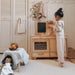 Child playing with a wooden play kitchen set in a room with light-colored walls and flooring.