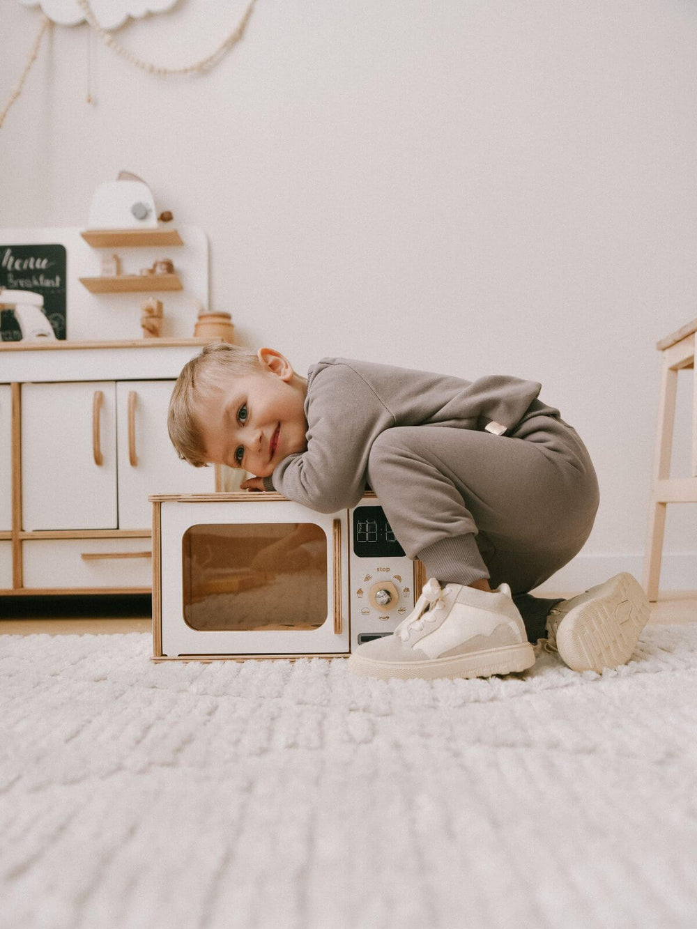 Child in a playroom with toy white wooden microwave on the floor with child leaning over the top