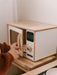 Child opening a white play microwave with wooden frame on a wooden stand.