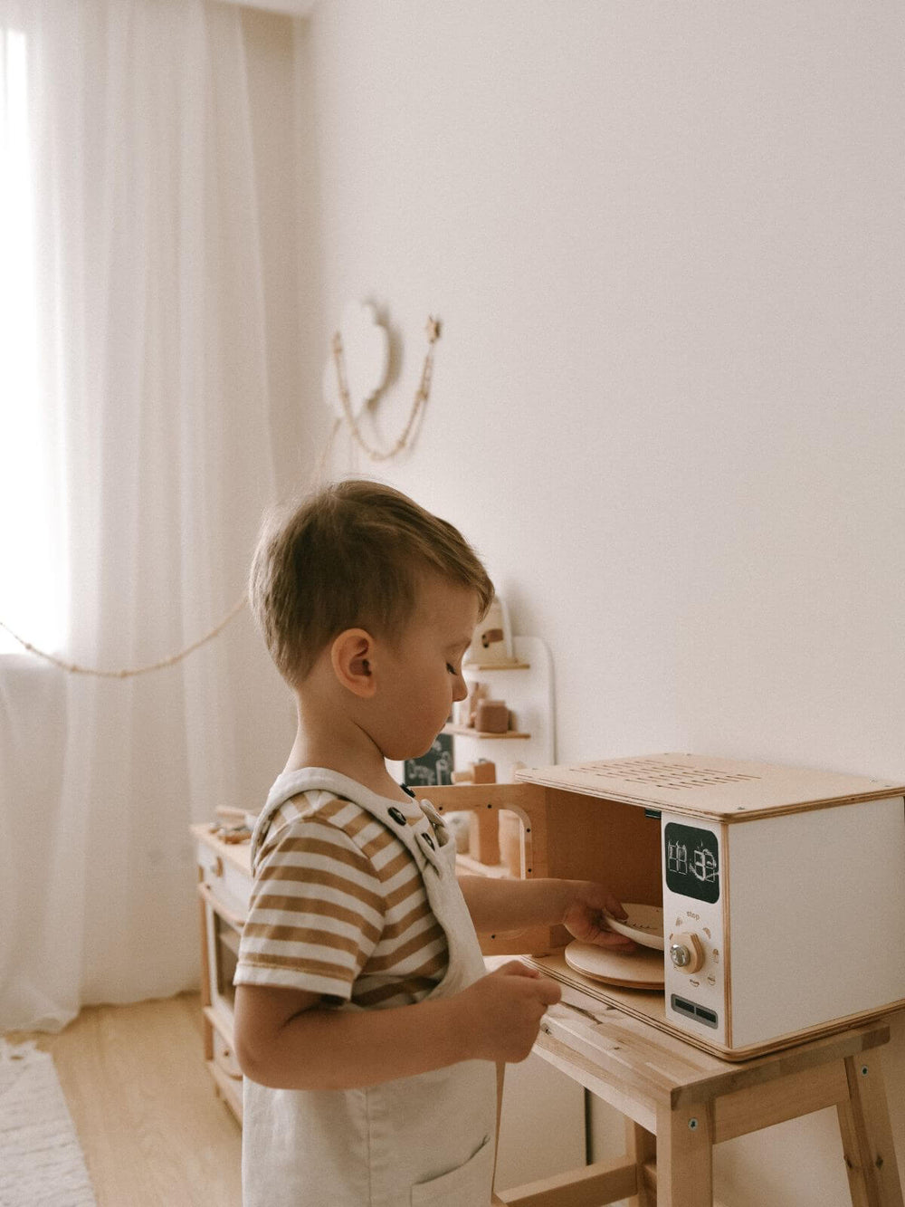 Child playing with a toy microwave in a bright room