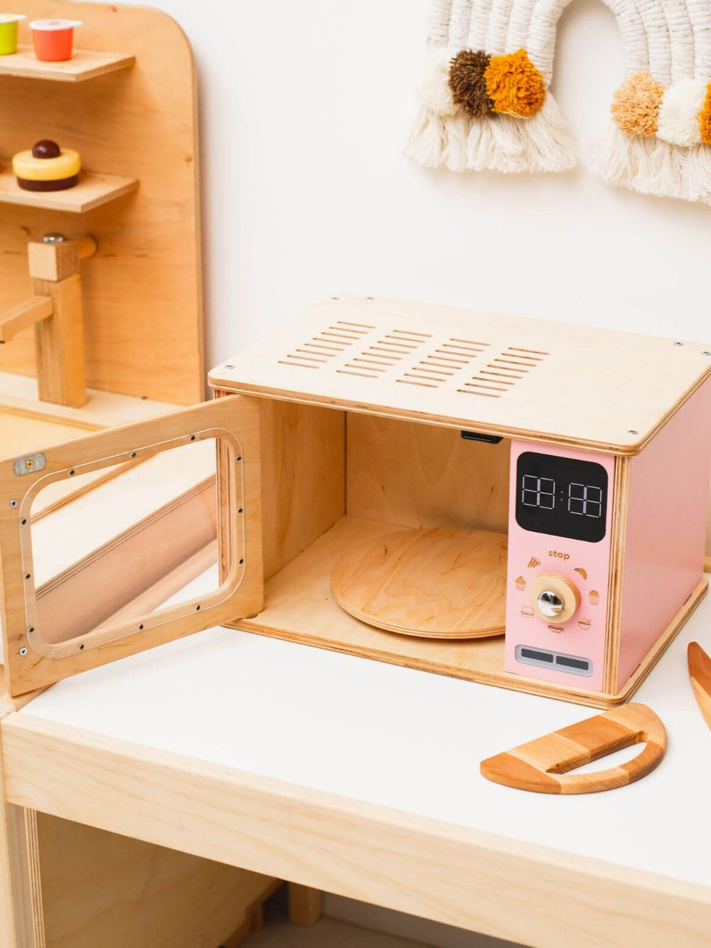 Wooden toy kitchen set with a pink microwave and digital clock on a white surface.