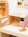 Wooden toy kitchen set with a pink microwave and digital clock on a white surface.