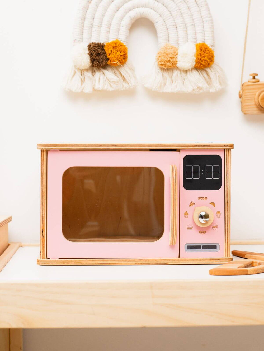 Pink microwave oven on a wooden surface with decorative items in the background.