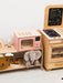 Children's play kitchen set with wooden stove, oven, and microwave on a white floor.