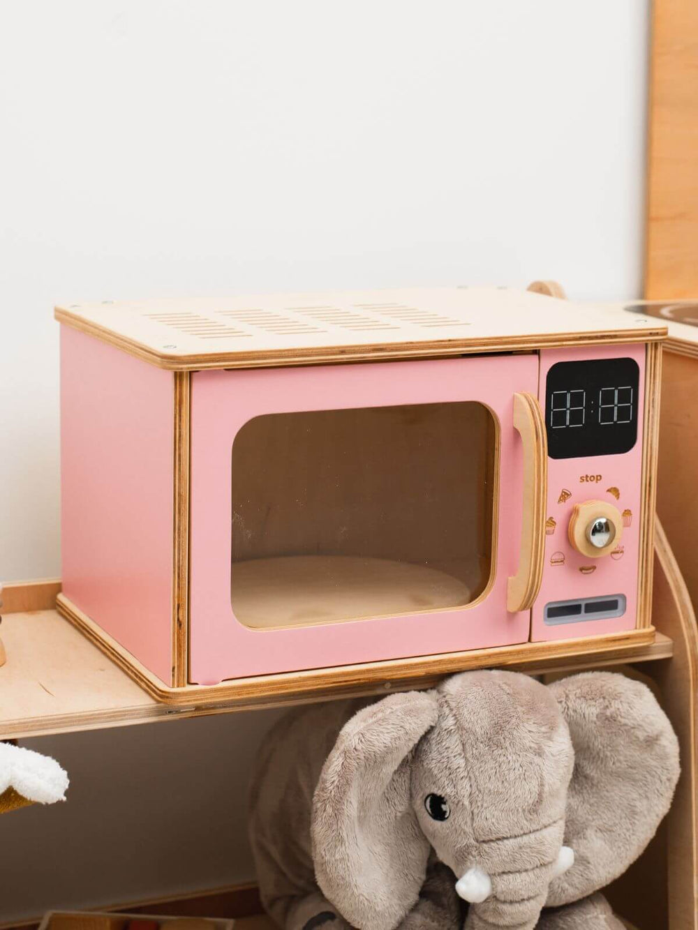 Pink toy microwave oven with wooden accents and a plush elephant toy on a white background
