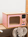 Pink toy microwave oven with wooden accents and a plush elephant toy on a white background