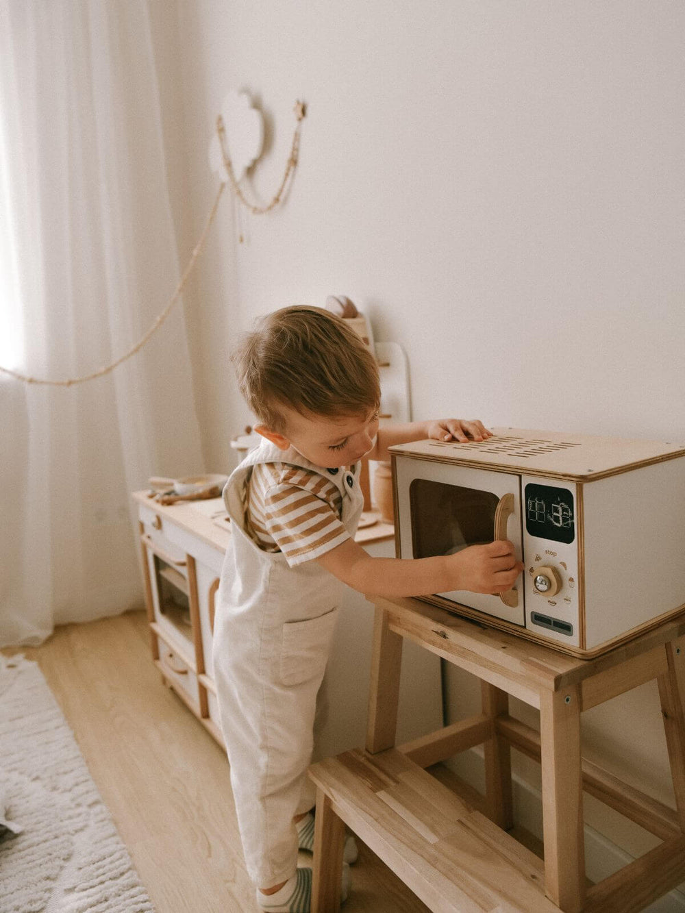 Child in a playroom playing with a white wooden toy microwave