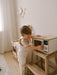 Child in a playroom playing with a white wooden toy microwave