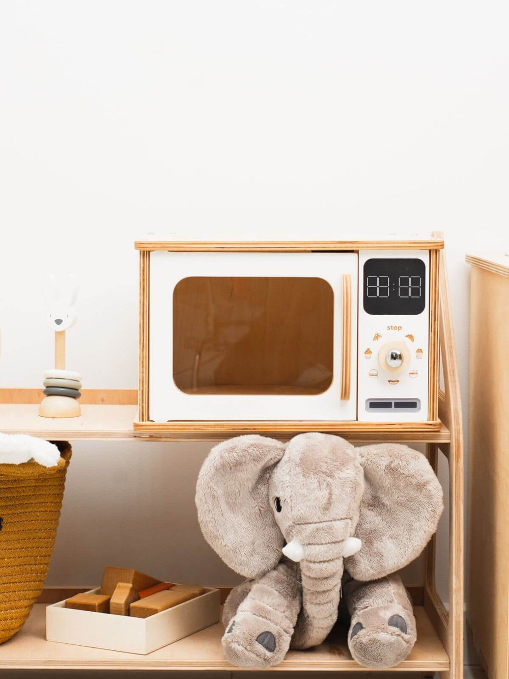 White wooden play microwave on a play shelf with a stuffed elephant below