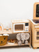 White wooden play microwave surrounded by toys on a shelf in a playroom
