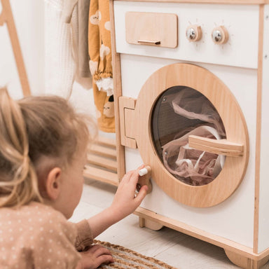 Child playing with a wooden toy washing machine in a room.