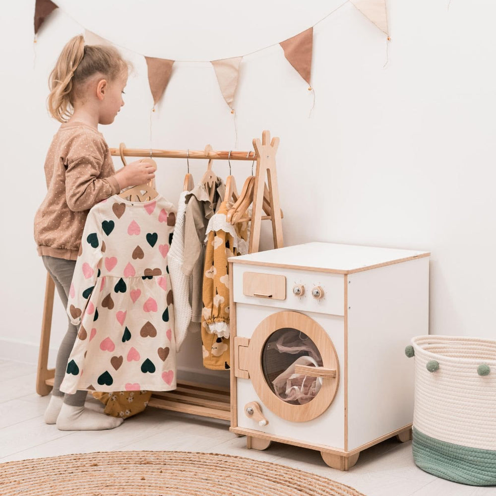 Child playing with a wooden play washing machine and clothes rack in a room.