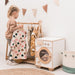 Child playing with a wooden play washing machine and clothes rack in a room.