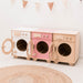 Wooden toy washing machine set on a white floor with a woven rug.